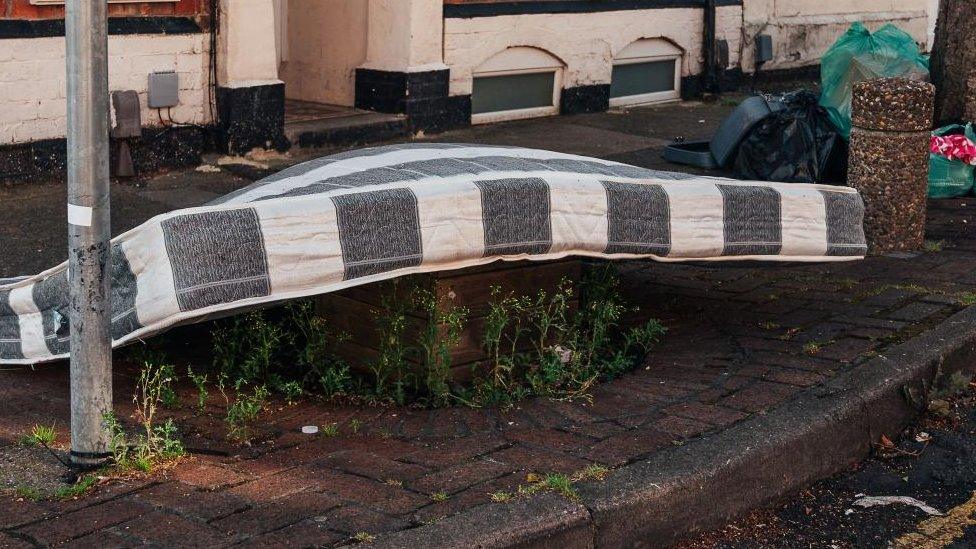 Black and white mattress lies outside a terraced house