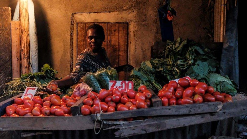 A woman makes a selection of the most expensive tomatoes for a customer just before the 7PM curfew in Kibera, Nairobi on May 05, 2020.