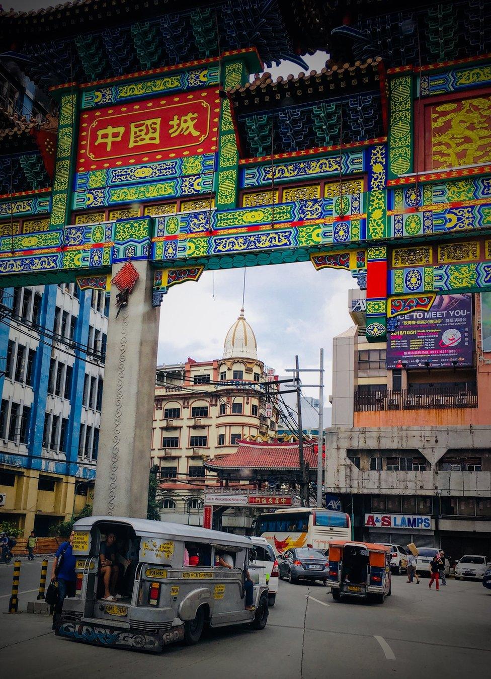 Cars drive under a colourfully decorated arch in Manila