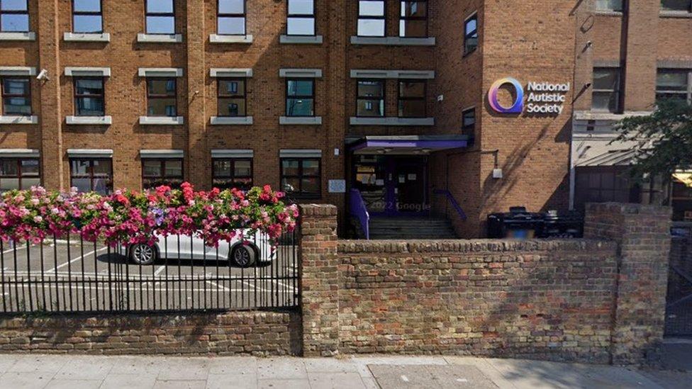 Three-storey brick building with small square windows. Sign reads: "National Autistic Society"