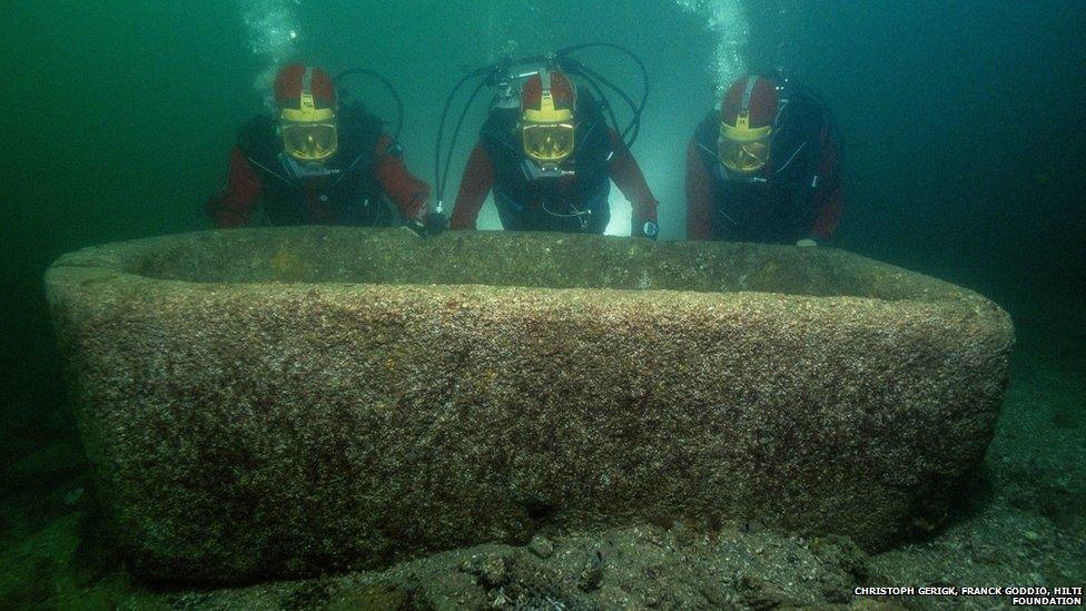 Diver archaeologists pose beside a large vat thought to have originally been located in a garden.