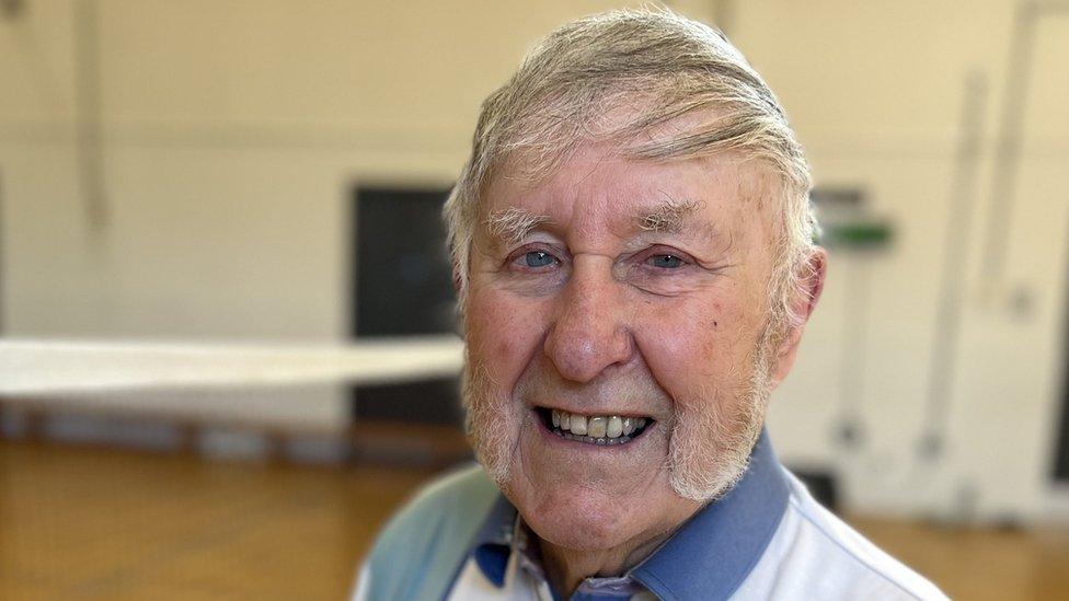 Colin Bedford smiles at the camera while standing on a badminton court