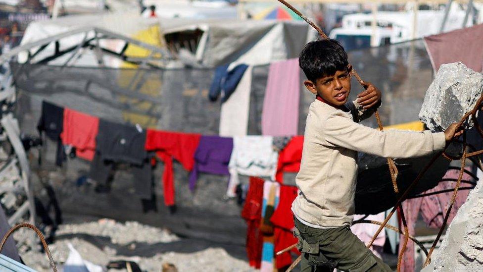 A displaced Palestinian child, part of a group who fled their homes due to Israeli strikes, looks out near rubble, at a tent camp, amid the ongoing conflict between Israel and the Palestinian Islamist group Hamas, in Rafah, southern Gaza Strip, December 29, 2023. REUTERS/Ibraheem Abu Mustafa