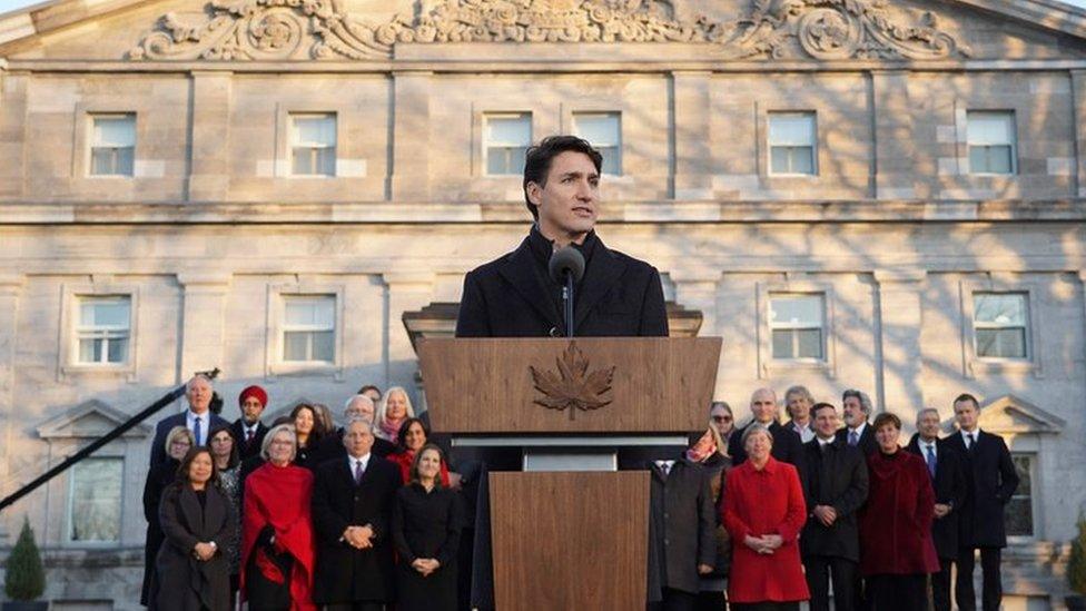 Prime Minister Justin Trudeau at a podium with his new cabinet standing behind him