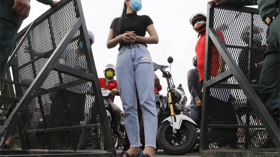 A pedestrian stops in front of a police barrier on a street in Phnom Penh, Cambodia