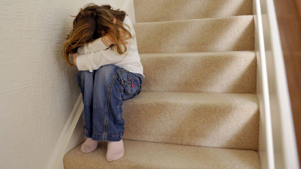 Child sitting on stairs with head in arms