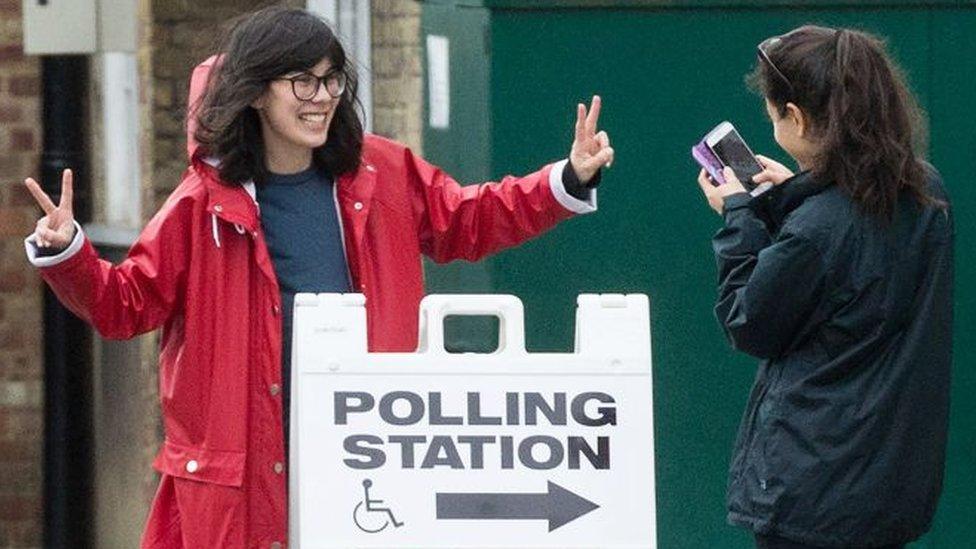 A woman photographs another outside a polling station