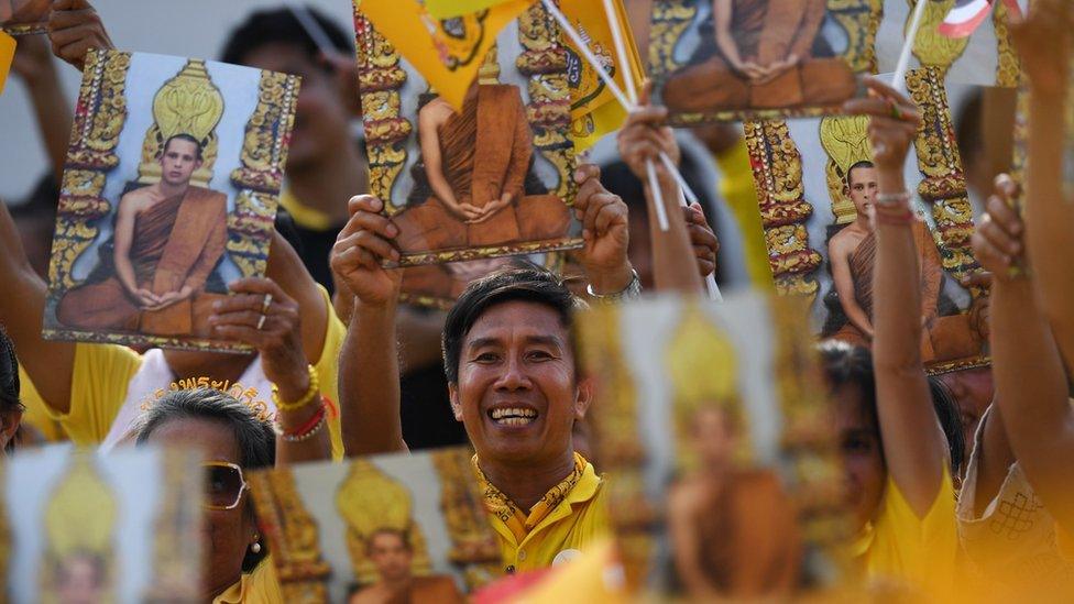 People hold portraits of the King as they wait for him and Queen Suthida to appear