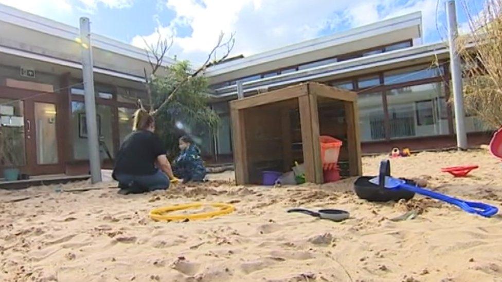 Child and adult in a sandpit in an outdoor area of a school building - buckets and spades are nearby