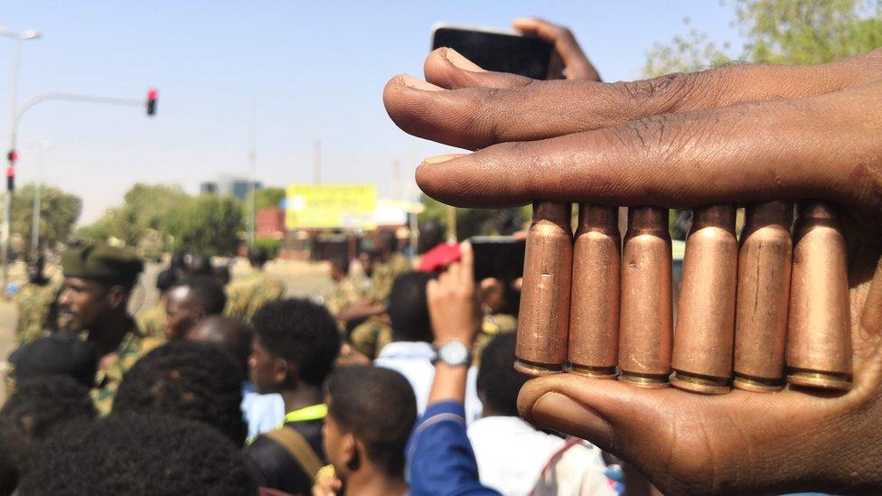 A Sudanese protester shows bullet cartridges as others gather in front of security forces during a demonstration in the area of the military headquarters in the capital Khartoum on April 8, 2019.