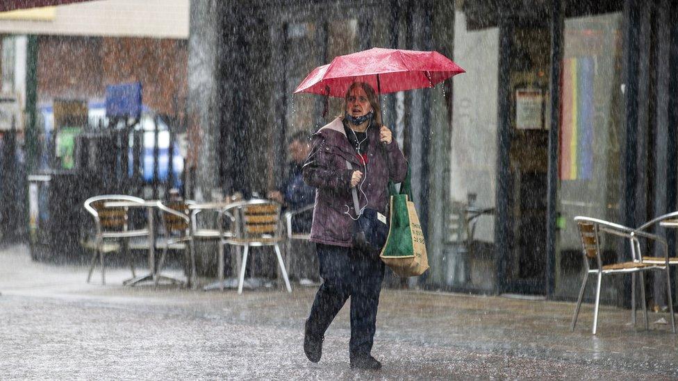 A woman shelters under an umbrella during a heavy downpour of rain in Belfast. Picture date: Monday July 31, 2023.