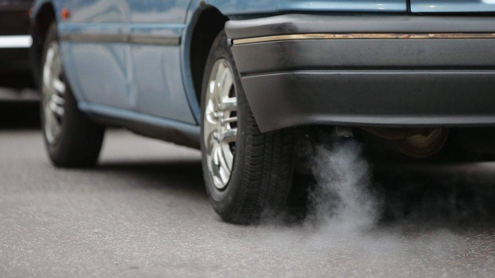 The exhaust pipe of a blue car with white smoking coming out.