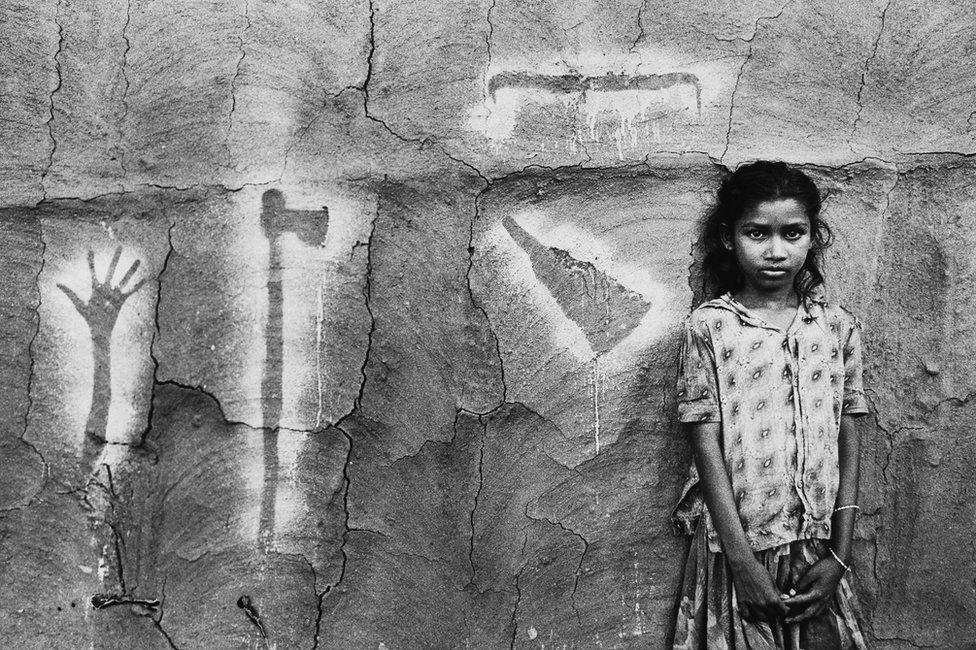 Child with traditional wall painting on the exterior of a house in Gujarat