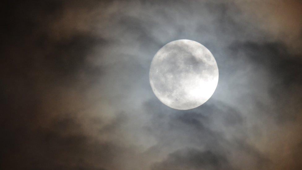 The full moon appears through the clouds