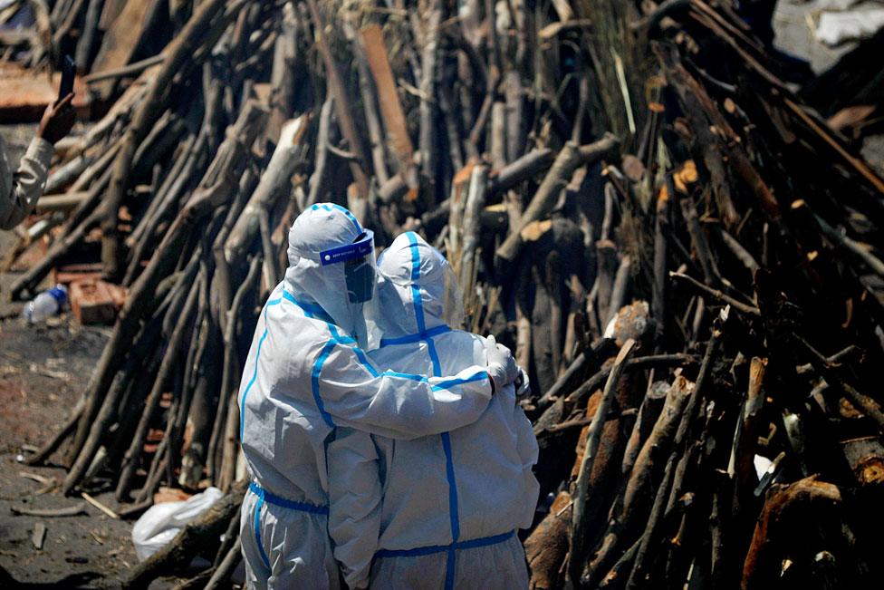 Relatives wearing PPE kit (Personal Protection Equipment) mourn next to funeral pyres at a crematorium in New Delhi, India