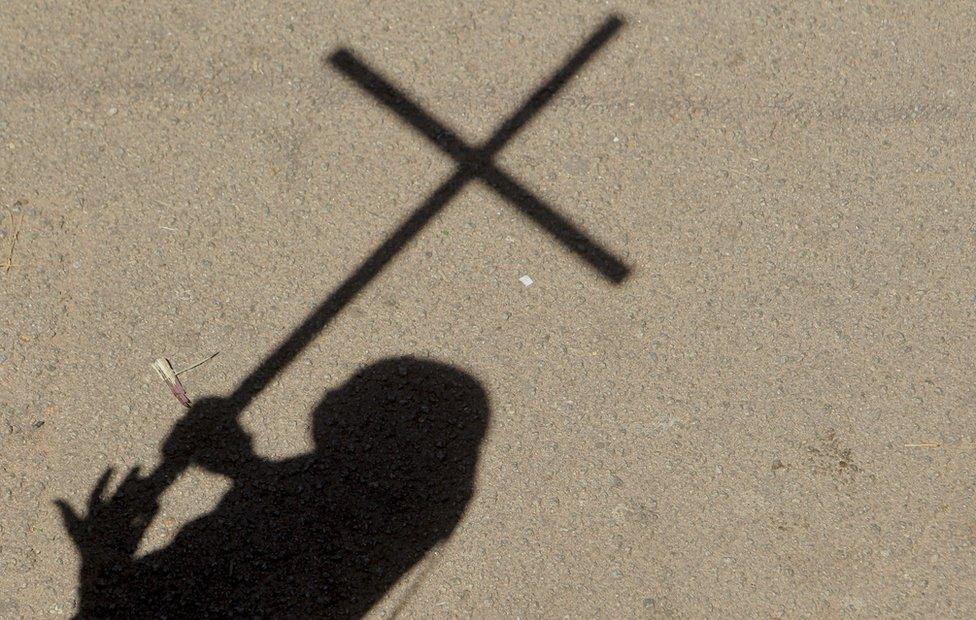 A woman casts her shadow as she holds a cross during a march in Harare, Zimbabwe, Wednesday, May, 18, 2016. Dozens of people marched in Zimbabwe’s capital Harare protesting the introduction of what they described as anti-Christian policies in public schools