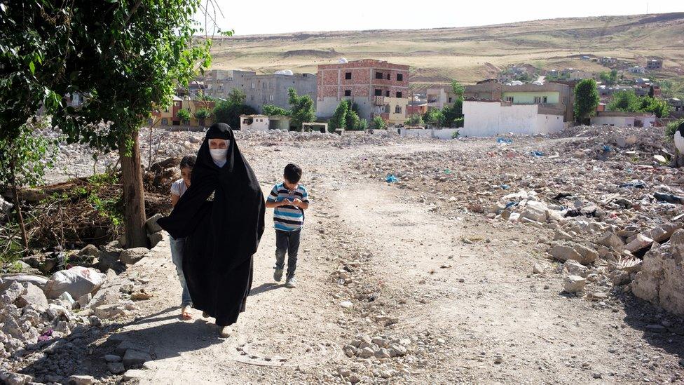 Woman walks with her two children along a street in Cizre, Turkey - May 2016