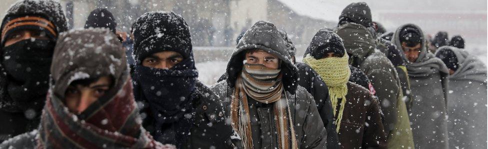 Migrants wait in line to receive free food during a snowfall outside a derelict customs warehouse in Belgrade (9 Jan)