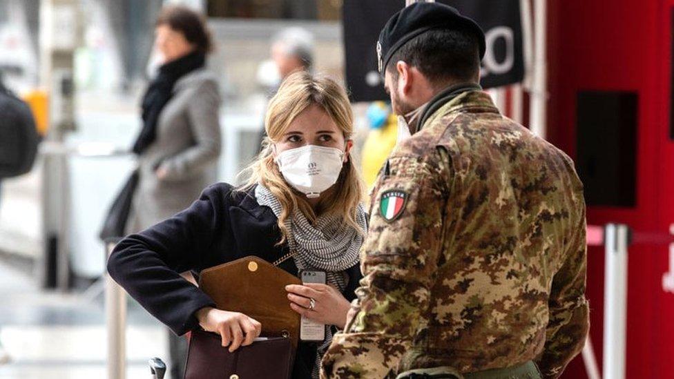 A woman wearing a face mask speaks to a soldier