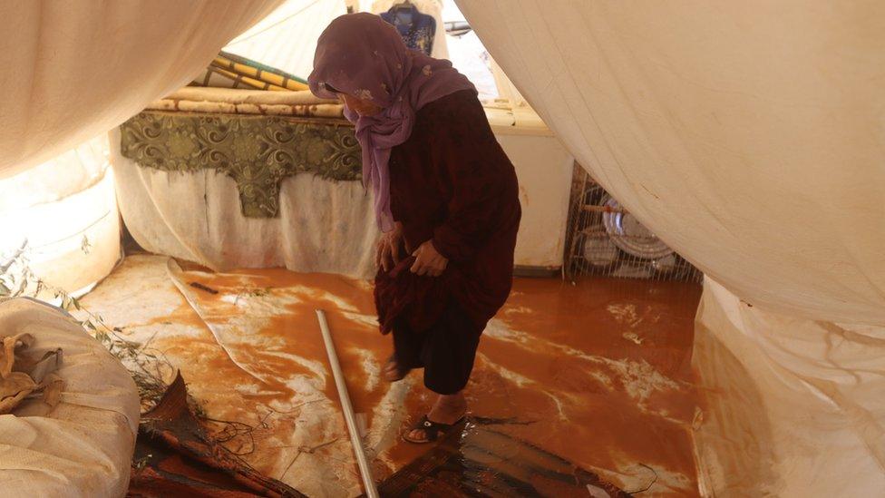 A woman stands in her flooded tent in Idlib province, Syria