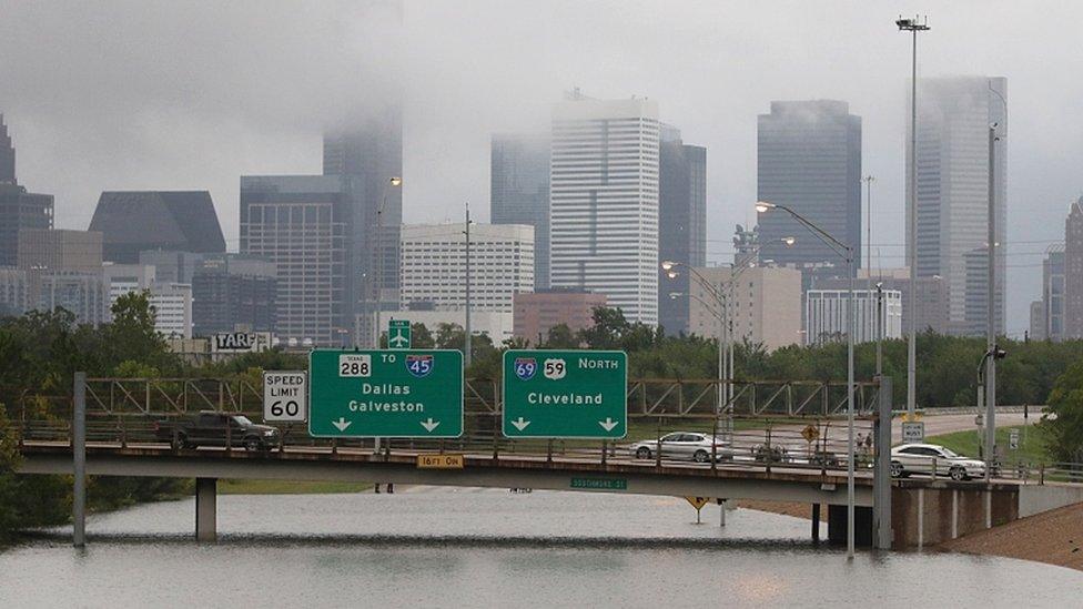 The city is pictured beneath clouds as a whole highway is overwhelmed by flood waters almost reaching the over-road signage