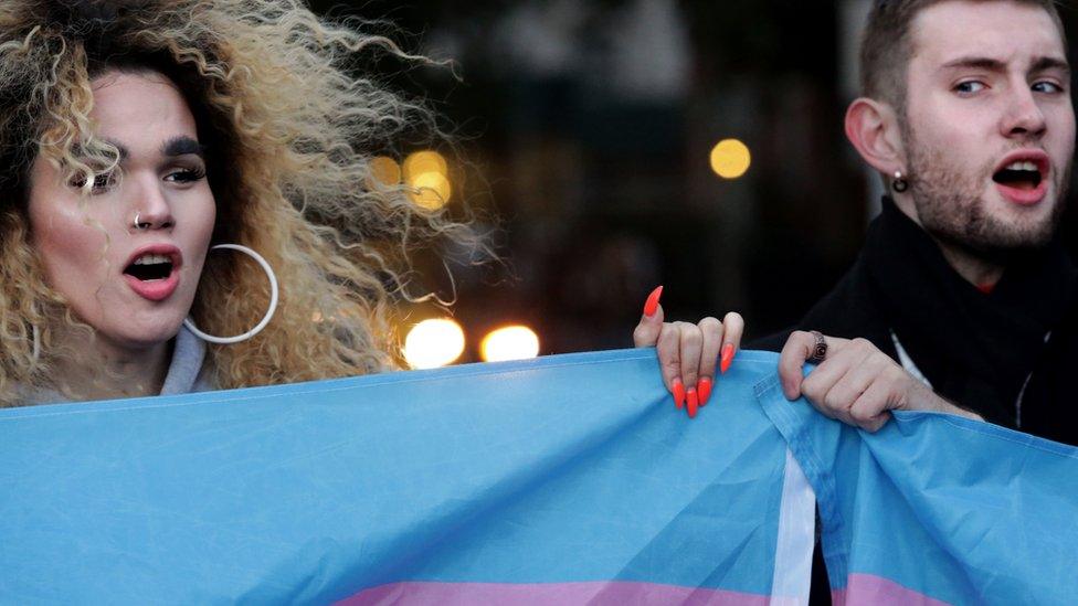 Two protesters hold up a flag for Transgender and Gender Non-comforming people