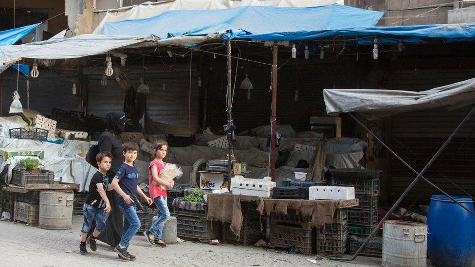 A woman and children walk past an empty vegetable market stall in rebel-held Aleppo (10 July 2016)