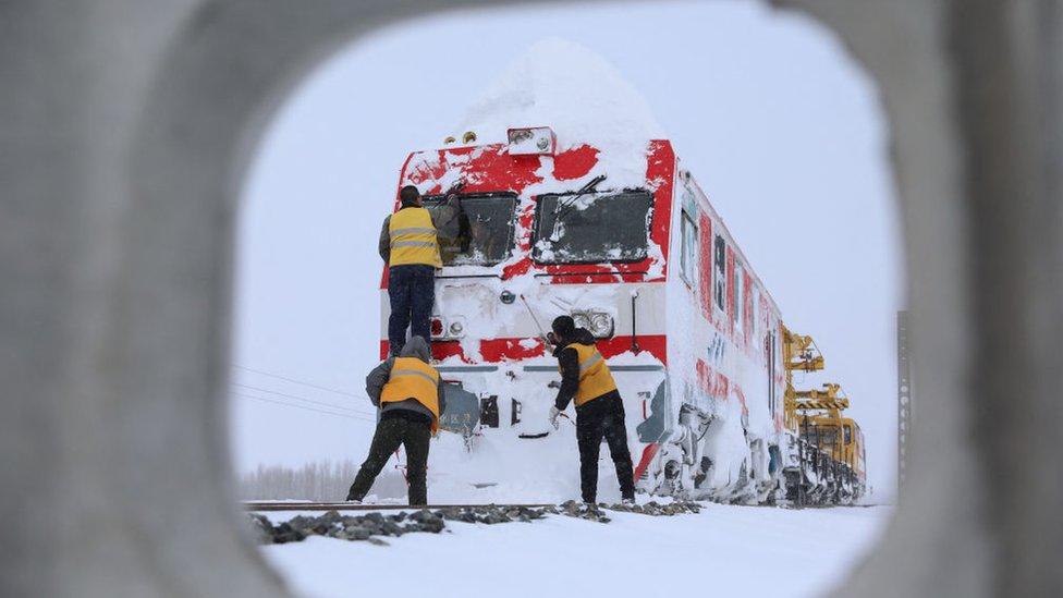 workers clean off a train covered in snow