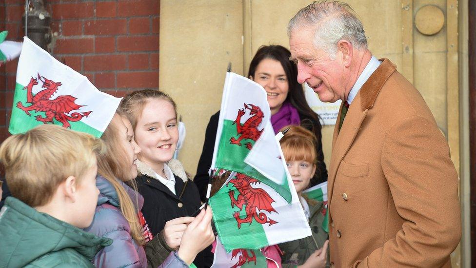 Children from St Cenydd and Cwm Rhymni schools wave Welsh flags as the Prince of Wales arrives for a visit to the Caerphilly Miners Community Centre in Caerphilly