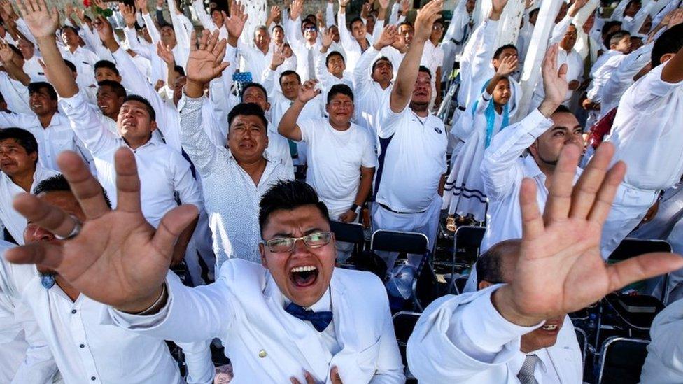 Men raise their hands and cry at an event held in Guadalajara by the Light of the World church.