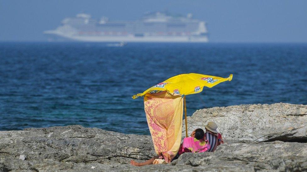 People shelter themselves from the sun under an umbrella in Mellieha, Malta, on June 25, 2021