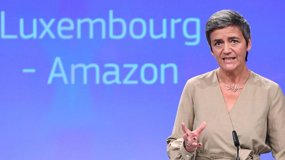 Margrethe Vestager addresses a press conference, with the words Luxembourg - Amazon on a screen behind her