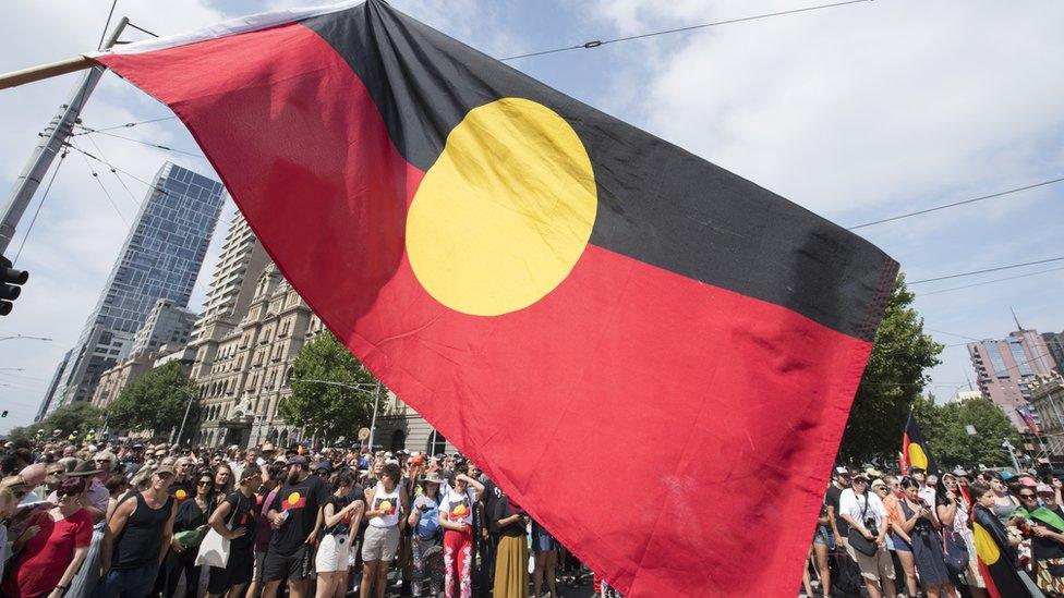 Protesters fly the Aboriginal flag over a march in Melbourne on Australia Day in 2019