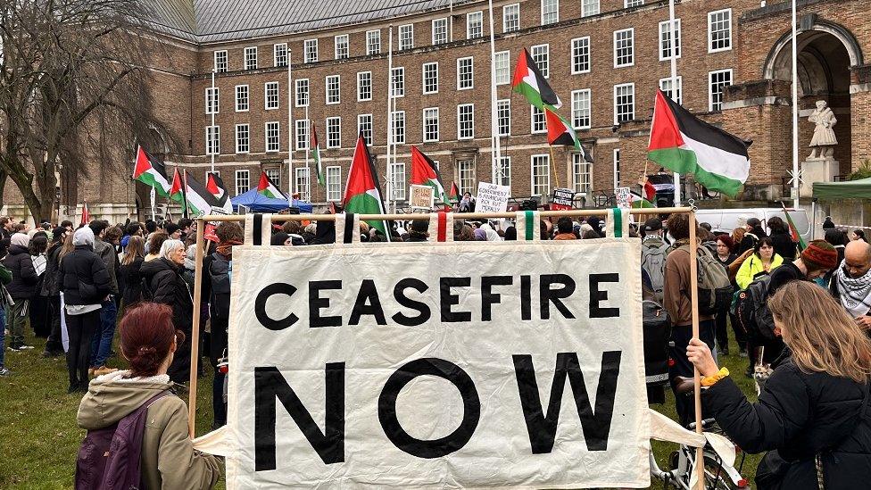 A protest in front of Bristol civic offices with a large 'Ceasefire Now' banner and Palestinian flags