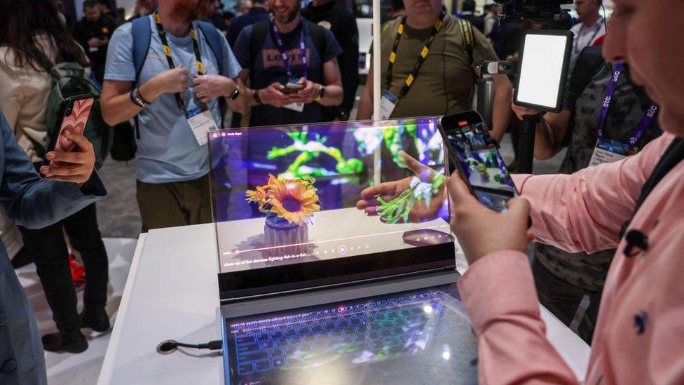 people at mwc look at a transparent laptop display - one person holds their hand behind the display while taking a picture