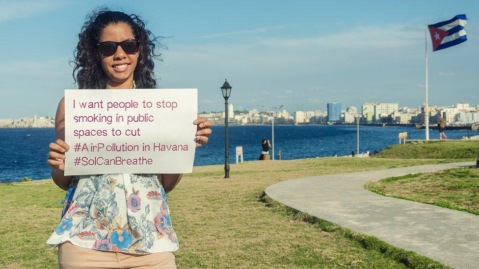 Mabel Oladle Azpiri holding up a sign saying "I want people to stop smoking in public spaces to cut #AirPollution in Havana #SoICanBreathe