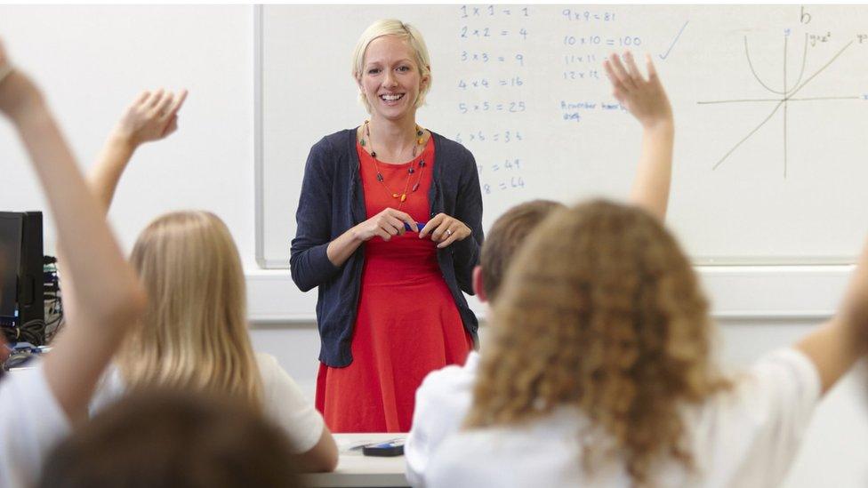 Female teacher and class with hands raised - stock photo