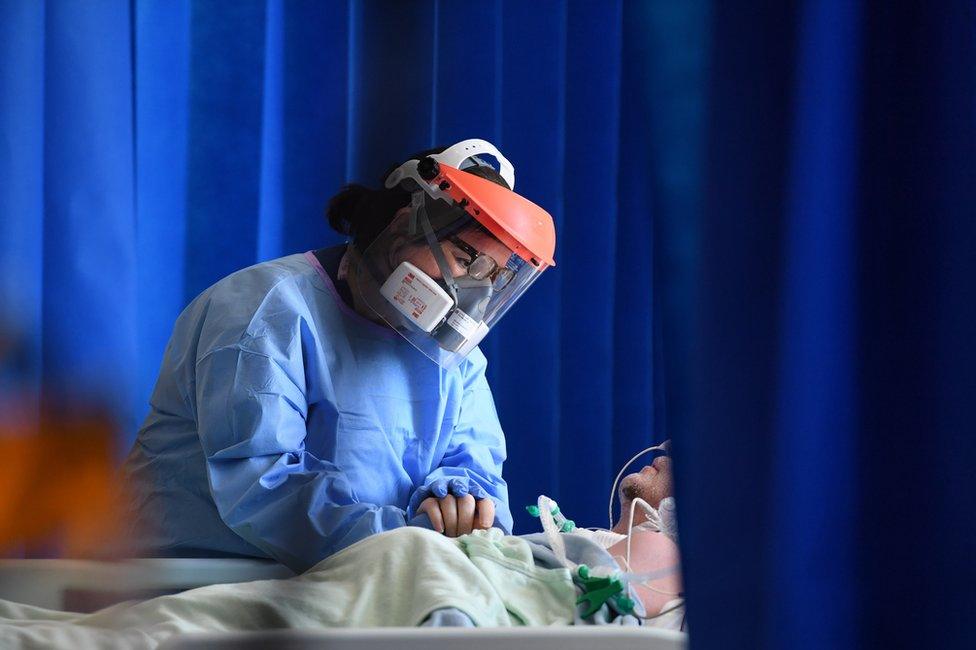 A clinical staff member holds the head of a patient whilst wearing PPE