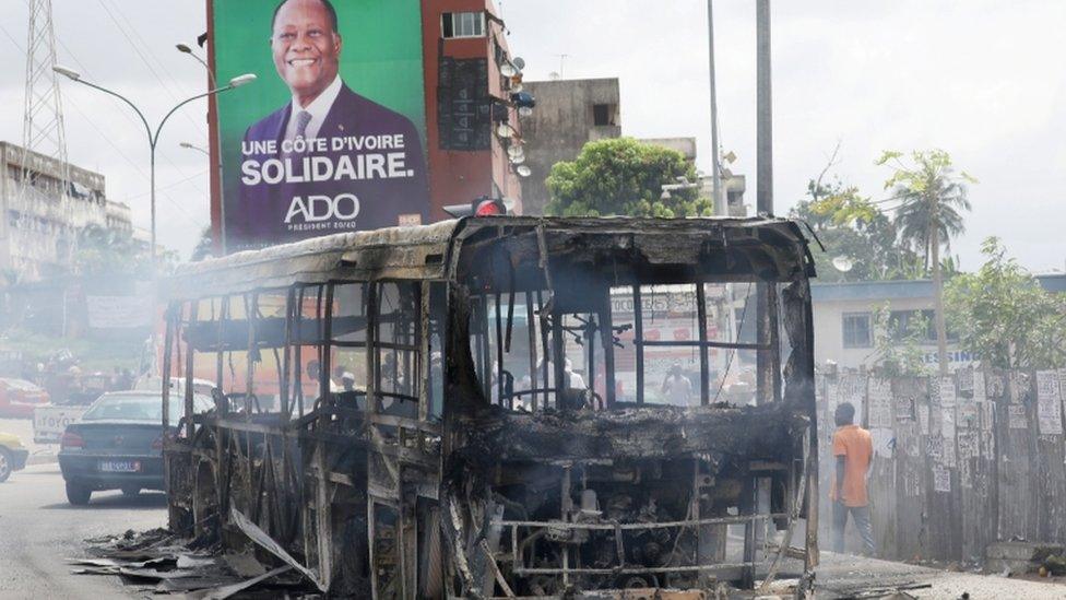 A campaign billboard of Ivory Coast President Alassane Ouattara seen behind a bus burned by protesters against his decision to stand for a third term, in Abidjan, Ivory Coast - 19 October 2020