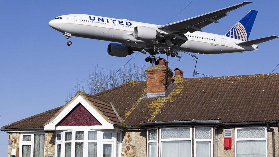 An aircraft flies over a house as it comes into land at Heathrow Airport in west London