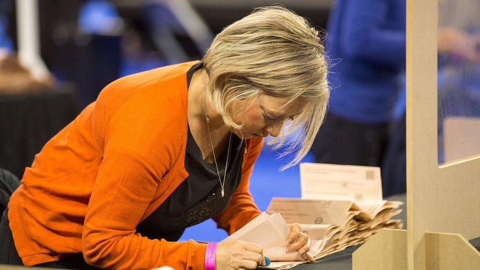 A woman counts peach coloured ballot papers