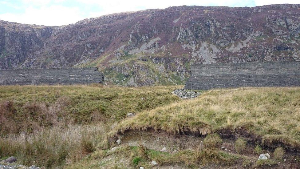 The breached dam wall with a visible gully cut by floodwater