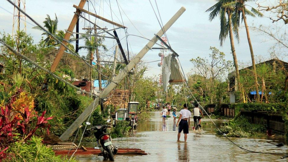 Residents walk past partially toppled electric posts after Typhoon Nock Ten hit Malinao, Albay in central Philippines