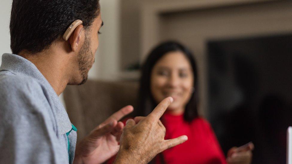 Deaf person with hearing aid signing to woman