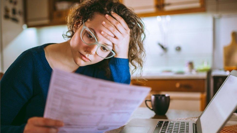 Young brunette curly female reading her bill papers, looking stressed