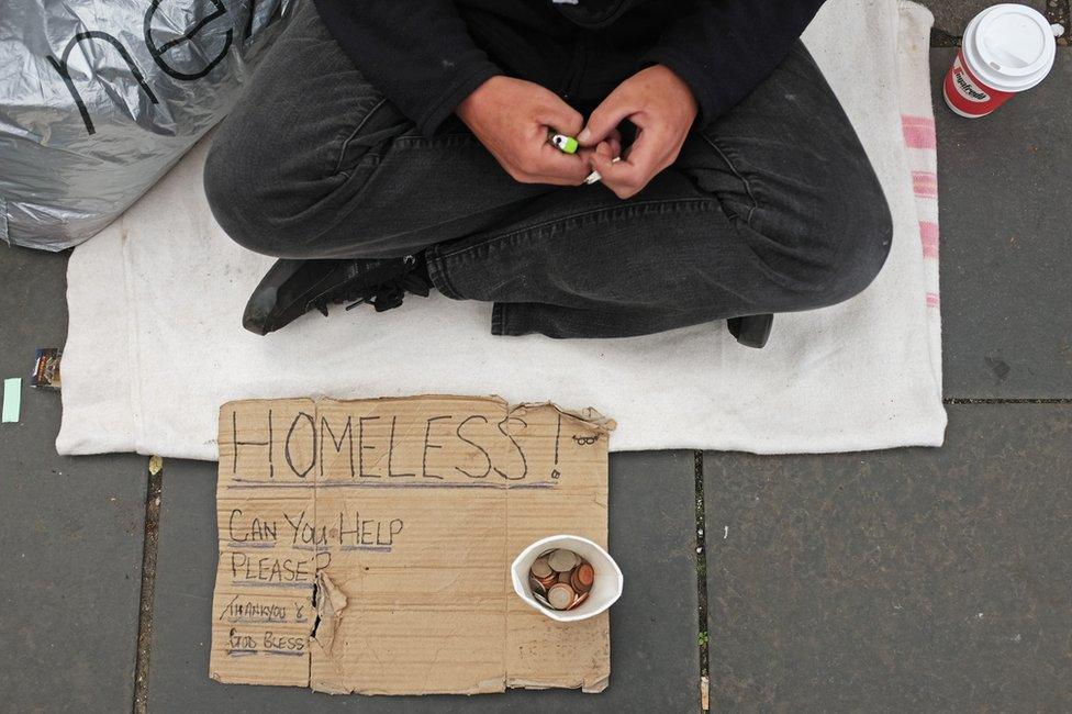 Hands, sign and money cup belonging to a homeless man