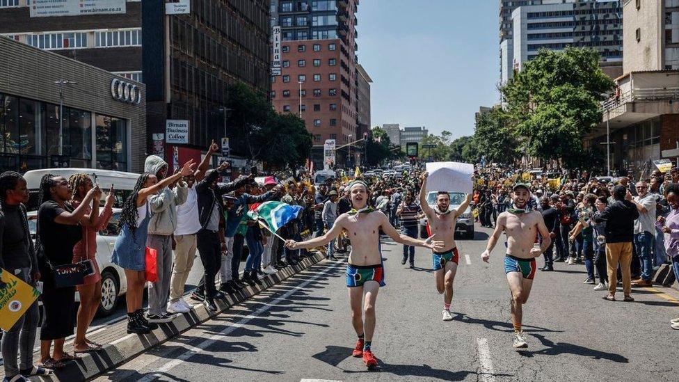 Supporters waving South African national flags and a placard run towards the Nelson Mandela Bridge during the Springboks Champions trophy tour in Johannesburg on November 2, 2023