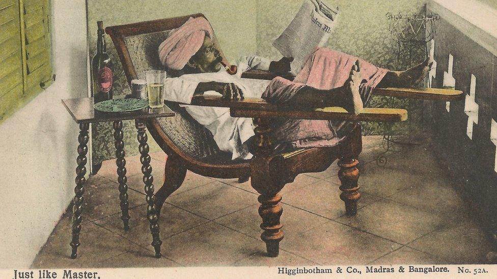 A picture postcard of an Indian man reading a newspaper while relaxing on a chair