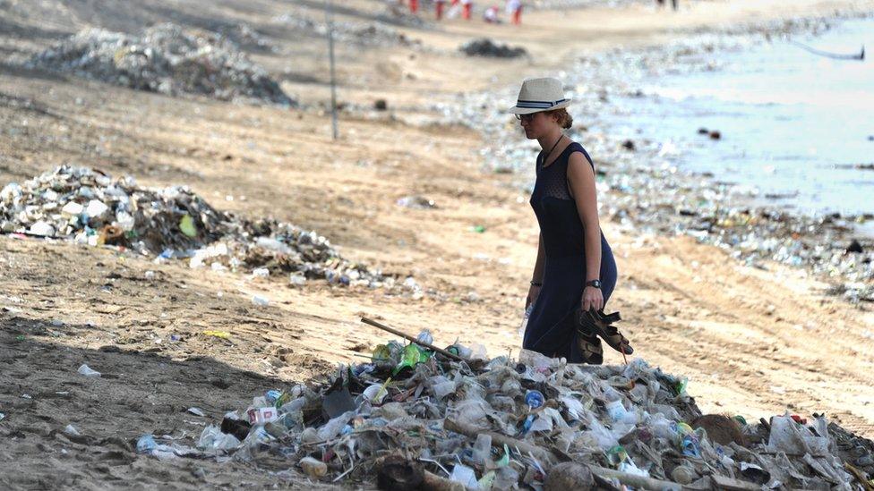 Tourist walks past rubbish on Kuta beach