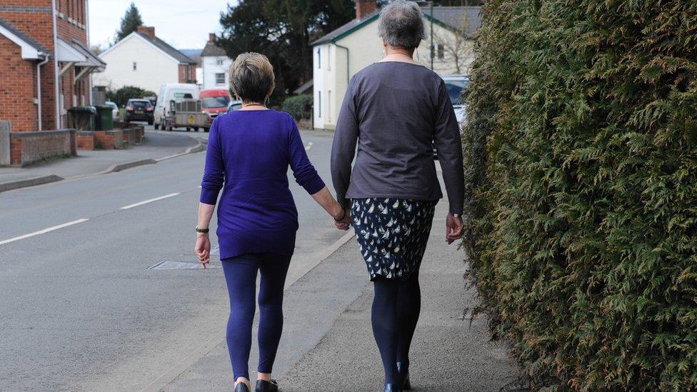 Penny and Lou walk down a road holding hands